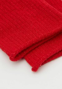 Tessuto lavorato a maglia rosso a coste con accenti metallici, caratterizzato da una texture morbida e bordi ripiegati, creando un aspetto stratificato.