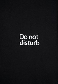Czarny materiał tekstylny z białym haftowanym napisem "Proszę nie przeszkadzać." Prosty wzór bez dodatkowych zdobień czy akcentów.