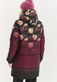 Květinový polstrovaný kabát v tmavém burgundském přechodu s růžovým a krémovým květinovým vzorem, připojenou kapucí a pletenou růžovou čepicí.
