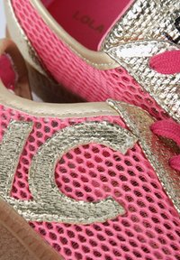 Baskets en mesh rose avec des accents dorés et un détail texturé. Comprend un logo proéminent, un matériau brillant et des lacets contrastés.