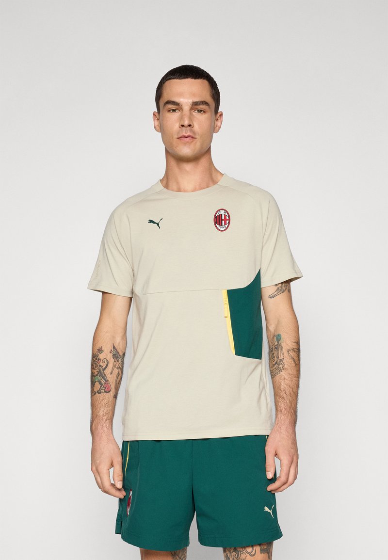Lys beige sports t-shirt med en grøn accentlomme, gul lynlåsdetalje og broderet logo. Korte ærmer og rund halsudskæring.