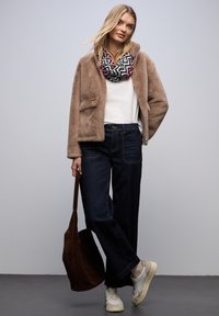 Beige faux fur jas, witte t-shirt, donkere wijde jeans, met een patroon zwarte en paarse sjaal, bruine schoudertas, witte sneakers.