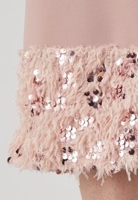 Vestido rosa claro com uma bainha fofa e texturizada, adornada com lantejoulas. O tecido é suave e as lantejoulas refletem a luz em tons de rosa dourado.