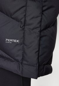 Svart isolerad jacka med en quiltad design, slät yta och Pertex Quantum-logotyp nära fållen.