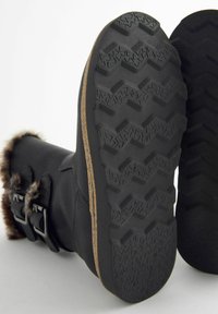 Schwarze, wasserdichte Stiefel mit Kunstfellakzenten, ausgestattet mit einer strukturierten Gummisohle und zwei Schnallen. Die Außensohle hat ein Zickzack-Profil.