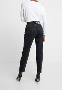 Černé džíny z denimu s rovně střiženými nohavicemi, designem s pěti kapsami a pasem s logem Calvin Klein. Nošeno s černými vysokými podpatky.