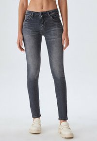 Jeans ajustados grises con un ligero desgastado, diseño de cinco bolsillos y cintura de altura media; combinados con zapatillas blancas sin cordones. Textura de denim suave.