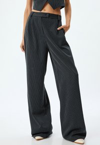 Gestreifte Hosen aus dunklem Stoff, mit hoher Taille, weit geschnittenen Beinen und Taschen. Die Streifen sind weiß vor dem dunklen Hintergrund.