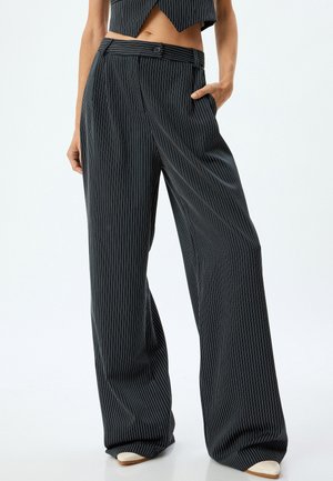 Pantalones a rayas de tejido oscuro, con cintura alta, piernas anchas y detalles de bolsillos. Las rayas son blancas sobre el fondo oscuro.