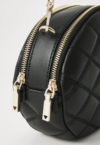 Borsa rotonda nera in faux pelle con texture trapuntata, zip e accessori in tonalità dorata. Presenta due scomparti con zip e una tracolla a catena.