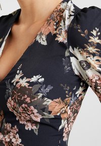 Floral patterned black dress with pink, white, and peach flowers, featuring a V-neck and slight puff sleeves on a person.