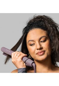 Lilla hårutdragare med rundade kanter och mönstrad grepp, med en professionell stylingsladd, hålls nära rakande hår.