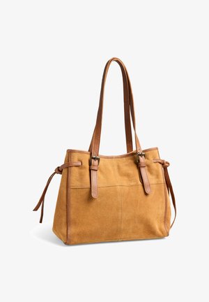 Sac à main en daim marron clair avec des lanières en cuir marron, des détails à boucle et des liens sur les côtés, présenté sur un fond blanc.