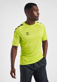 Camiseta deportiva de color amarillo neón con acentos en chevrón negros en los hombros, con cuello redondo y mangas cortas, hecha de material transpirable.