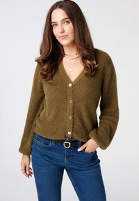 Olijfgroen, textuur cardigans met een V-hals, vijf voorknopen en lange mouwen. Gepaarde met blauwe jeans en een zwarte riem.