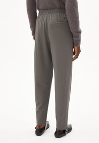 Grijze rekbare broek met een trekkoord in de taille, met een achterzak en een rechte pijpdesign. Draagt met zwarte schoenen.