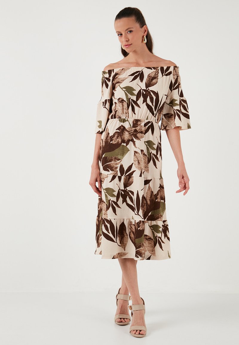 Robe décolletée en crème avec un motif de feuilles brunes et vertes, design en volants et tissu léger ; associée à des talons de couleur claire.