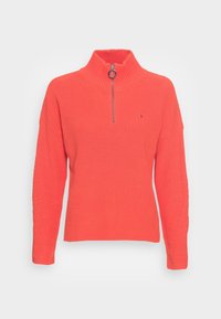 Stickad tröja i klar orange med hög hals och halvlång dragkedja. Har ett strukturerat mönster på ärmarna och en logga på bröstet.