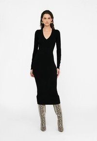 Zwarte langarmige jurk met v-hals, gemaakt van aansluitende stof, knielengte, gecombineerd met kniehoge laarzen met textuur en slangenprint.