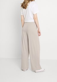 Beżowe spodnie o szerokich nogawkach wykonane z miękkiej tkaniny, z elastyczną talią i bocznymi kieszeniami. Ubrane z białym t-shirtem i sneakersami.