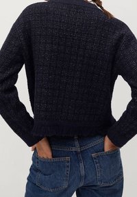 Pull court bleu marine avec un motif tissé texturé, fini par des franges à l'ourlet et des manches longues. Porté avec un jean en denim bleu.