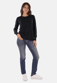 Maglietta nera a maniche lunghe in tessuto morbido, abbinata a jeans blu e sneakers bianche. L'outfit presenta una vestibilità rilassata e un design semplice.