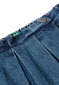 Modrý džínový materiál s nařaseným elastickým pasem, malá zelená cedulka a detail ve tvaru srdce z kovového knoflíku.