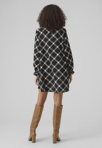 Melna un balta rakstainā kleita ar garām piedurknēm, brīvu piegriezumu, savilktām apkaklītēm un atslēgas formas aizmugures dizainu, kombinēta ar brūniem līdz ceļgaliem zābakiem.