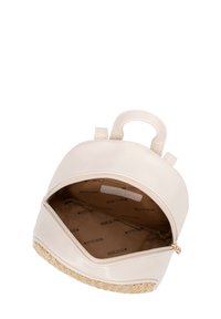 Mochila de imitación cuero beige con forma redondeada, cierre de cremallera y fondo tejido. El interior cuenta con un forro con un patrón de logotipos.
