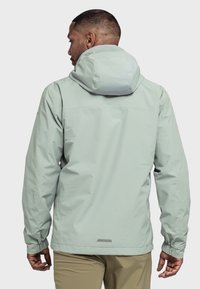 Hellgrüne wasserdichte Jacke mit Kapuze, elastischen Bündchen und einem eleganten Design mit einem reflektierenden Akzent auf der Rückseite.