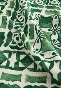 Tissu vert et blanc à motifs avec une surface texturée. Présente des formes géométriques et florales, des nuances de vert variées et un tissage visible.