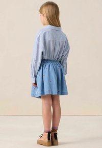 Chemise rayée bleue et blanche à manches longues et col, associée à une jupe en denim ornée de motifs de cœurs rouges et d'une taille élastique.