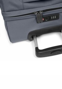 Valise à roulettes grise avec un extérieur texturé, deux zips, une serrure à combinaison intégrée et une poignée extensible.