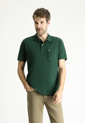 Polo verde con mangas cortas, cuello abotonado y un bolsillo en el pecho. Está hecho de una tela suave con una textura sutil.
