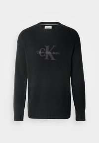Pull en maille noir à manches longues avec poignets et ourlet côtelés, présentant le logo "Calvin Klein Jeans" et "cK" en gris foncé centré sur la poitrine.