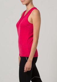 Dopasowany różowy bezrękawnik sportowy z lekkiego, gładkiego materiału. Posiada dekolt w serek i subtelną teksturę, w zestawieniu z czarnymi legginsami.