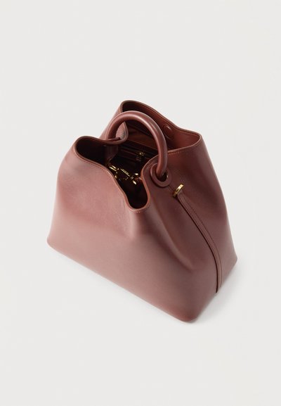 Απαλή τσάντα χειρός από δέρμα μωβ με στρογγυλεμένες λαβές, ανοιχτή κορυφή που αποκαλύπτει εσωτερική τσέπη με φερμουάρ και χρυσές λεπτομέρειες μεταλλικών εξαρτημάτων.