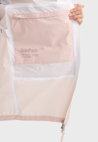 RainPack, lagana ružičasta tkanina s glatkom teksturom. Ima zatvoreni džep i bijele akcentne detalje. Dizajniran za kompaktno skladištenje.