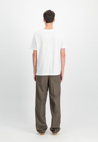 Λευκό βαμβακερό T-shirt με κοντά μανίκια, σε συνδυασμό με χαλαρούς ελαιοπράσινους παντελόνες. Απλός σχεδιασμός, χωρίς ορατά μοτίβα ή διακοσμήσεις.