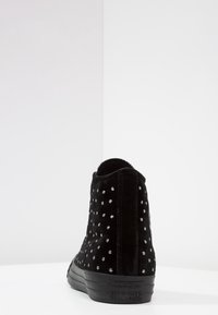 Svart mockaskor med silvernitar, hög topp-design, texturerad yta och gummisula med "Converse All-Star"-logotyp.