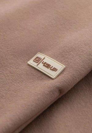 Brązowa tkanina o miękkiej teksturze, z kremową prostokątną metką wytłoczoną z napisem "LEVEL UP" w brązowym kolorze.