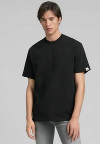 T-shirt nera con scollo a girocollo in tessuto di cotone, con maniche corte, taglio dritto e un piccolo logo sul petto. Etichetta discreta sulla manica.