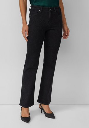 Donkerblauwe flare jeans van denim met subtiele glinsterende versieringen, vijf zakken en riemlussen, gecombineerd met zwarte pumps met puntige neus.