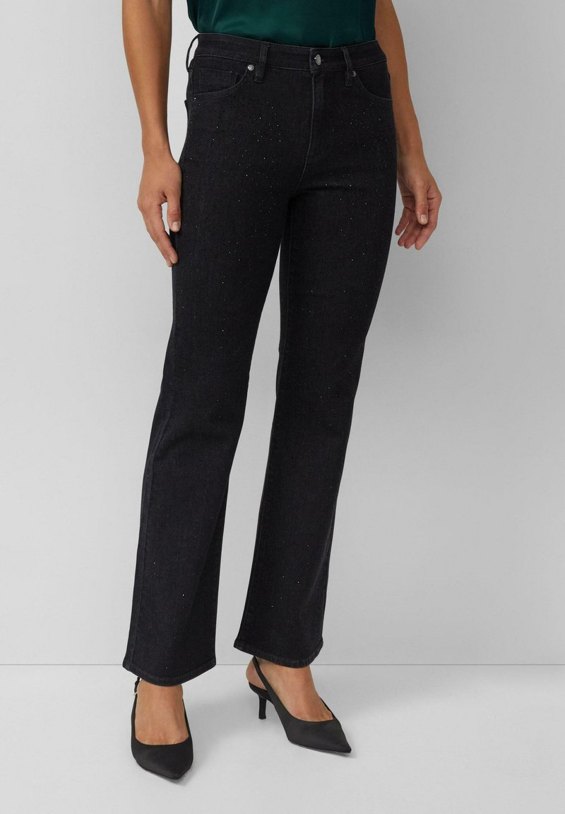 Jean évasé en denim foncé avec des embellissements subtils scintillants, cinq poches et passants pour ceinture, assorti à des escarpins noirs à bout pointu.