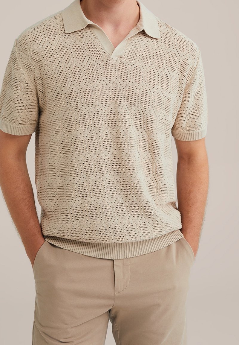 Beige knitted polo shirt with a diamond pattern, short sleeves, and a textured finish, paired with light beige trousers.