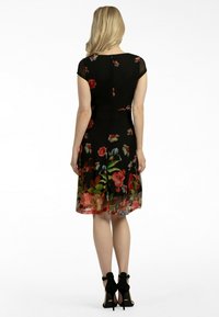 Vestido negro con estampado floral, mangas cortas, capa transparente, corsé ajustado y falda acampanada que llega hasta la mitad de la pantorrilla. Combinado con tacones negros.