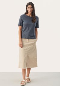 Tamsiai mėlyna trumpa rankovė t-shirt, derinama su smėlio spalvos iki kelių sijonu su priekinėmis plyšiais. Atsitiktiniai sandalai užbaigia ansamblį.
