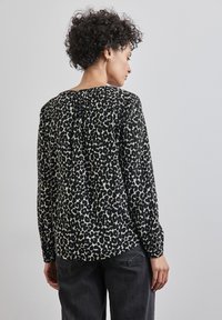 Blusa a maniche lunghe in stampa maculata nera e crema. Tessuto leggero, scollatura rotonda e dettaglio posteriore leggermente arricciato.