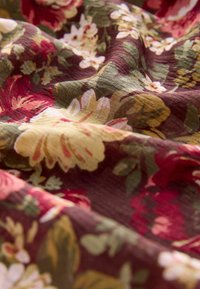 Material floral cu un fundal bordeaux închis; prezintă flori mari galbene și roz, frunze verzi și o suprafață texturată, ușor mototolită.