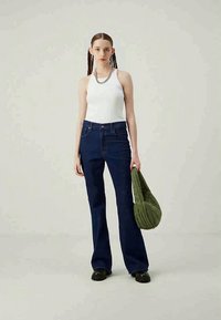 Kék farmer, harangszárú nadrág magas derekkal, fehér ujjatlan toppal párosítva. A modell egy sötétzöld, steppelt válltáskát tart. Fekete cipő.